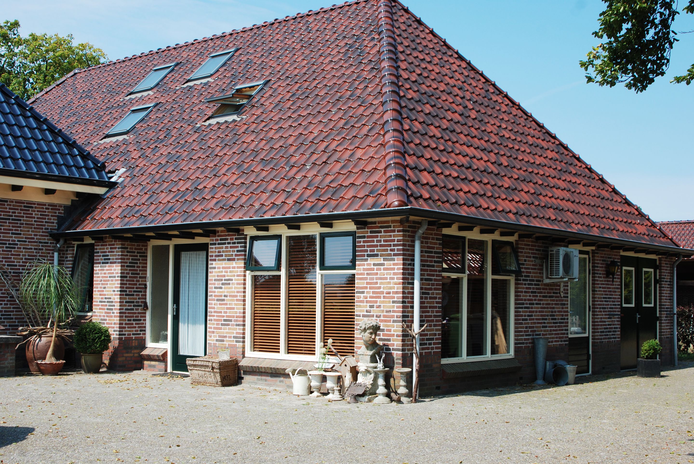 Et toetages murhus med rødt tegltag, store vinduer og et lille haveområde med plantekrukker.