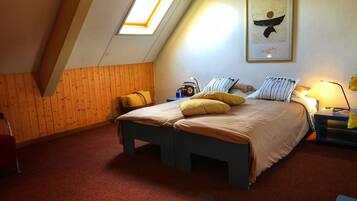Un dormitorio con techo inclinado, una cama con almohadas amarillas, una obra de arte enmarcada en la pared y una mesita de noche con una lámpara.