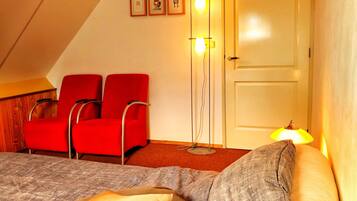 Een kamer met een bed, twee rode stoelen, een vloerlamp en een deur.