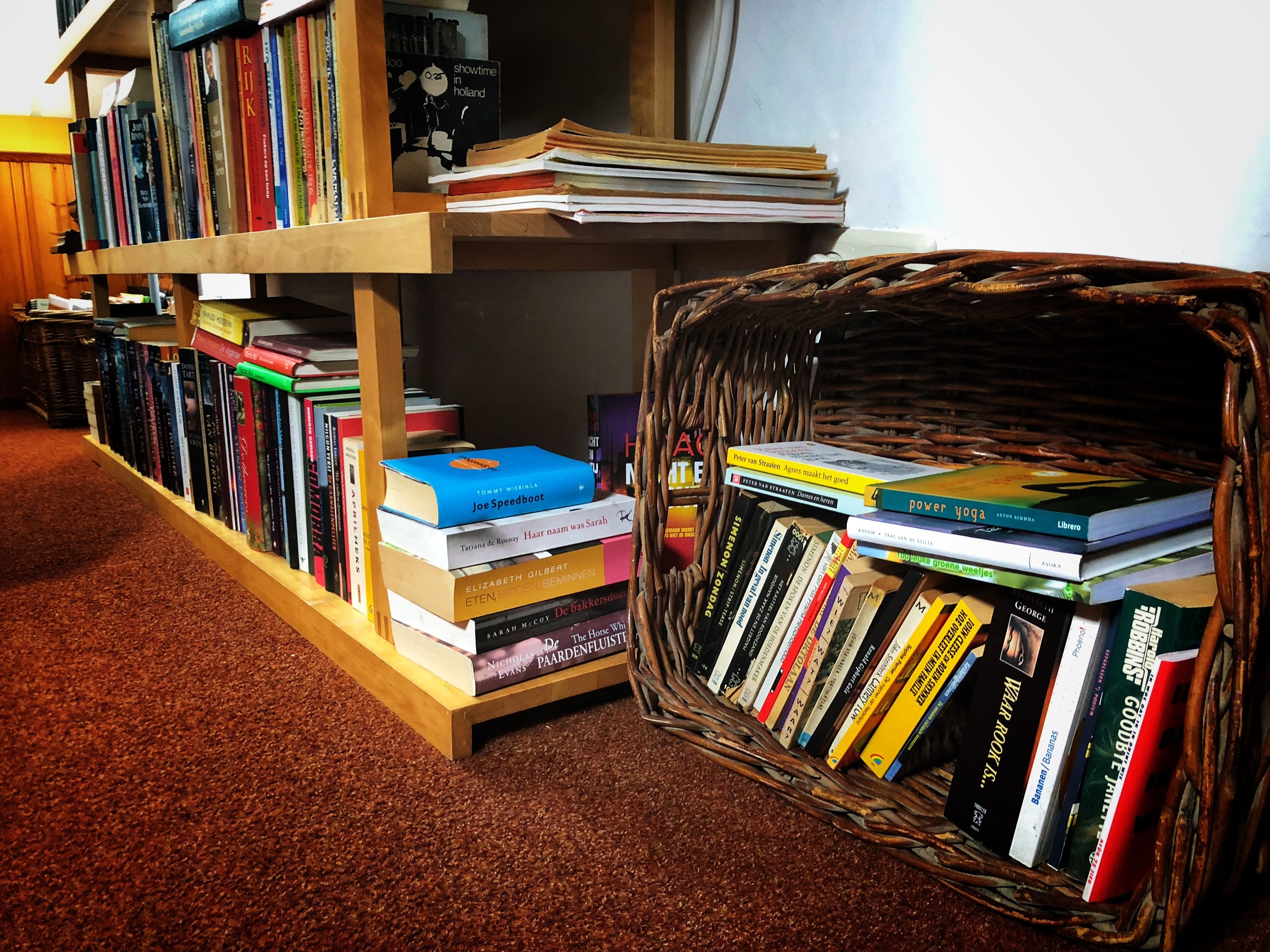 A bookshelf filled with books and a wicker basket containing more books.