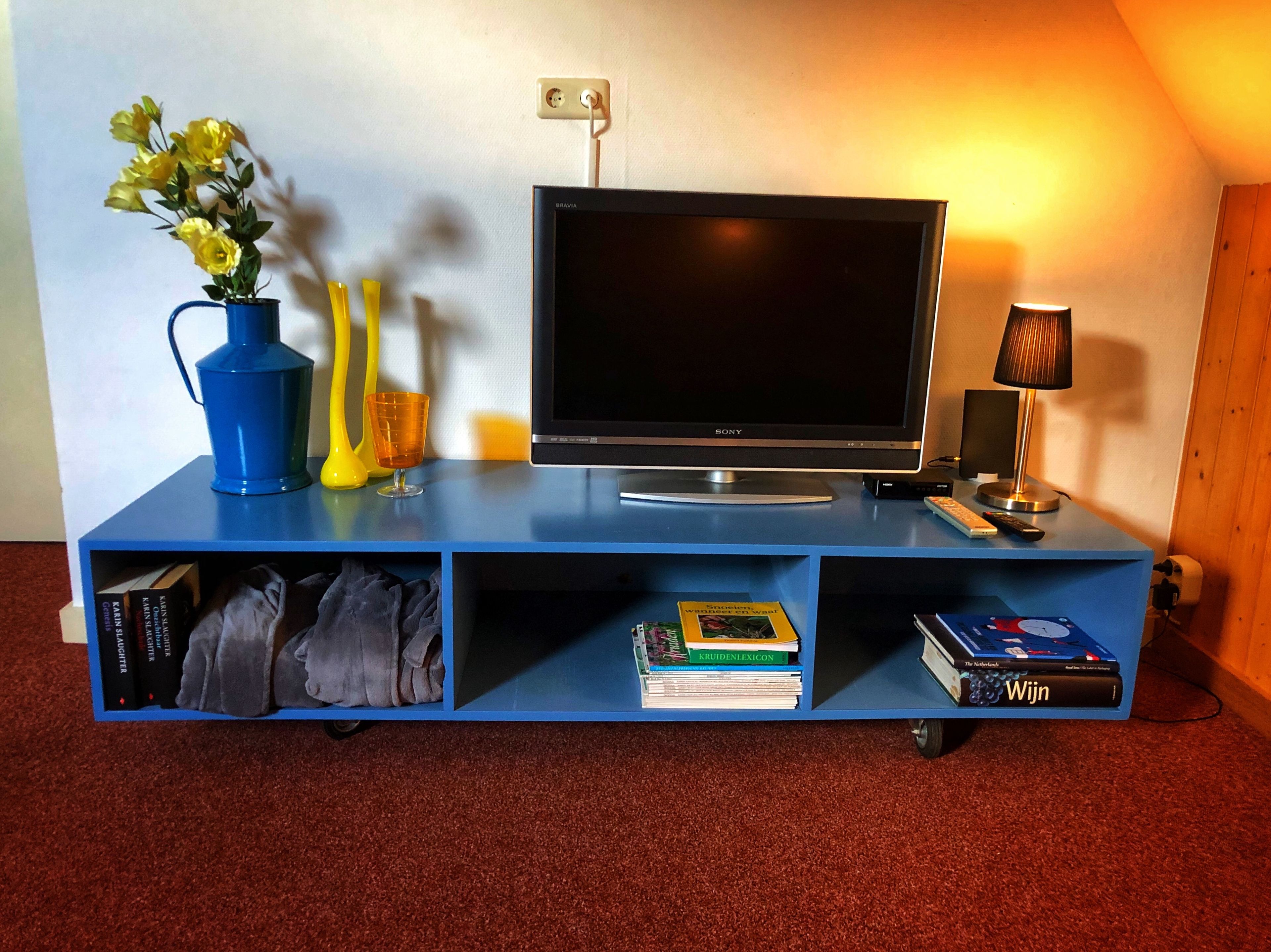 Un mueble azul de entretenimiento con un televisor de pantalla plana, una lámpara y un florero con flores.
