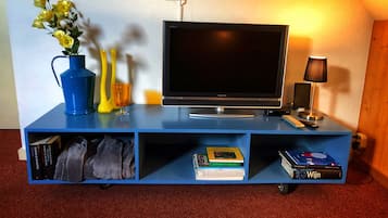 Un mueble azul de entretenimiento con un televisor de pantalla plana, una lámpara y un florero con flores.