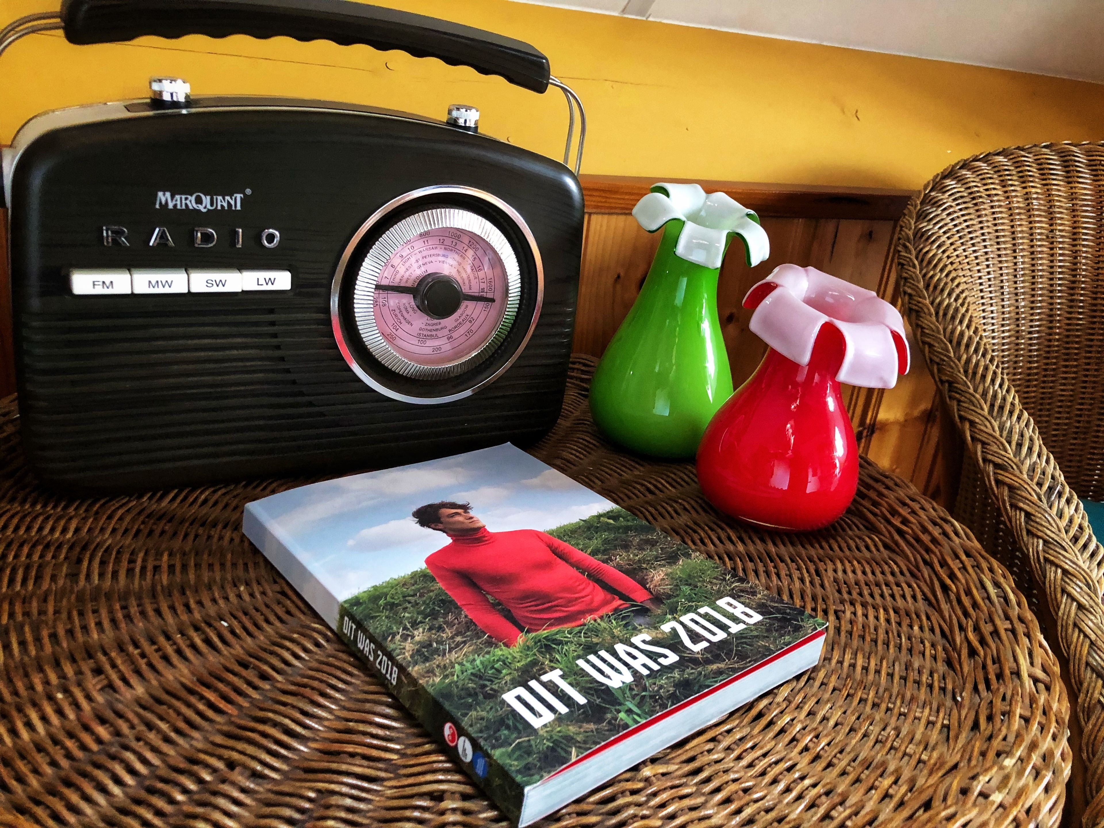 A Marquint radio, a book titled "It Was 2018", and two spray bottles on a wicker chair.