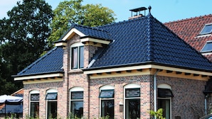 A brick building with a steeply pitched roof and multiple windows. - B&B Zandhuizen (Zandhuizen)