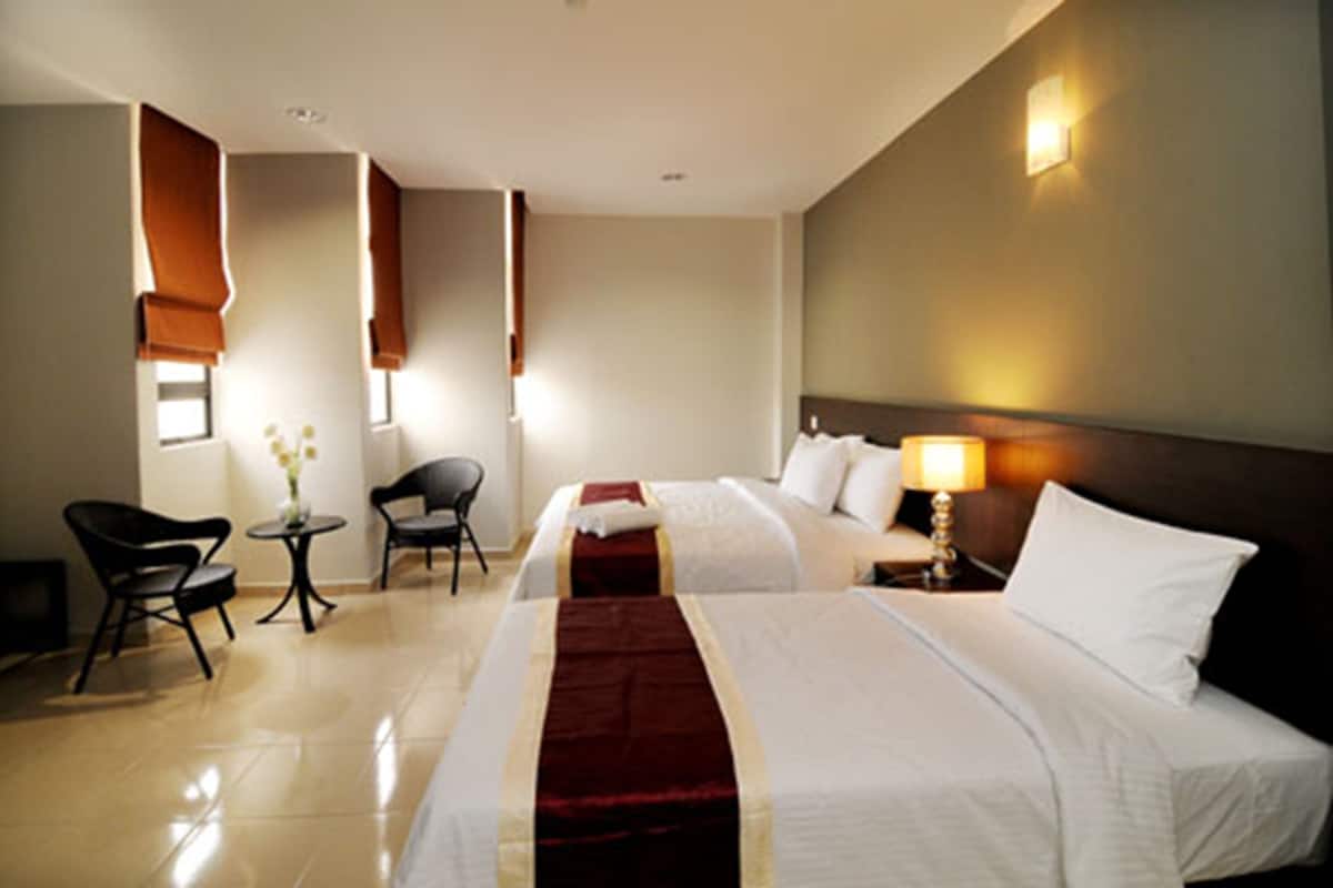 A hotel room with two beds, a sitting area with chairs, a small table, and a lamp.