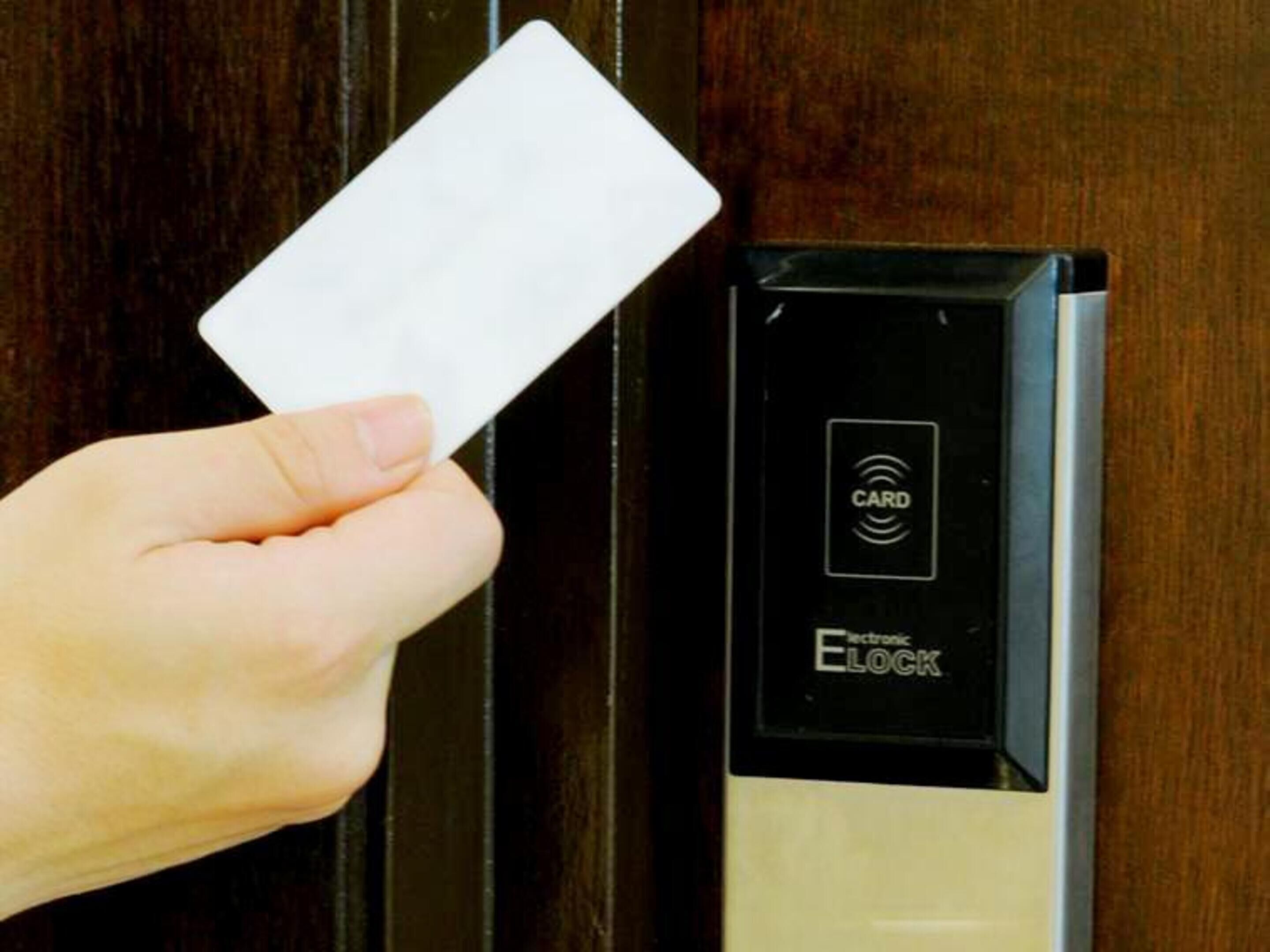 A hand holding a card near a door with an electronic lock mechanism.