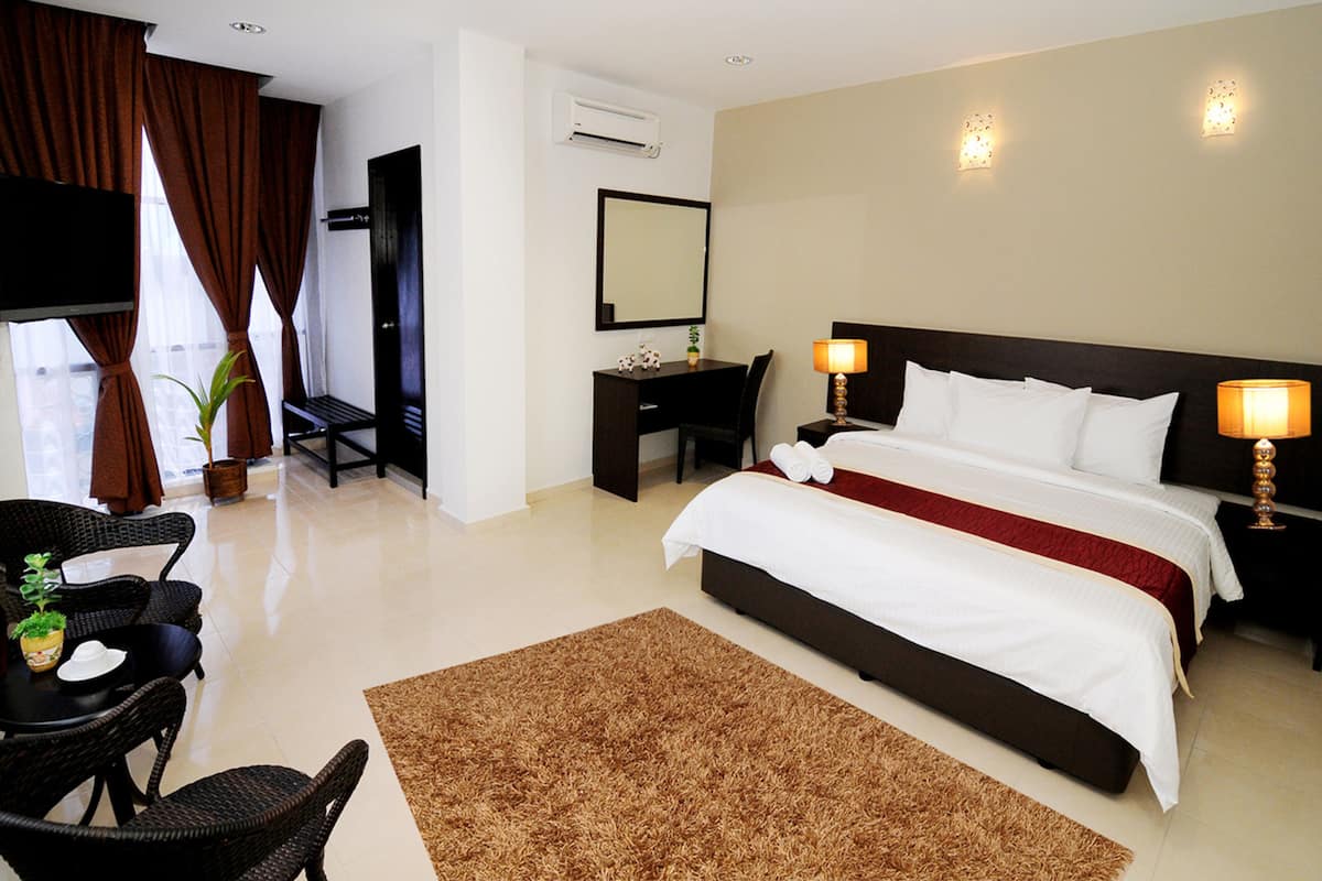 A hotel room with a large bed, a desk, a chair, a TV, and a window with curtains.