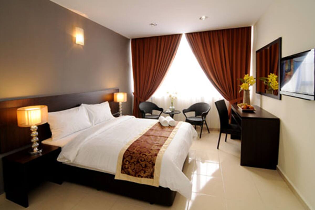 A hotel room with a large bed, a desk, two chairs, a small table, and a lamp.