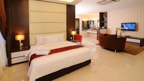 Quarto de hotel moderno com uma cama grande, televisão, área de estar e banheiro visível por uma porta aberta.