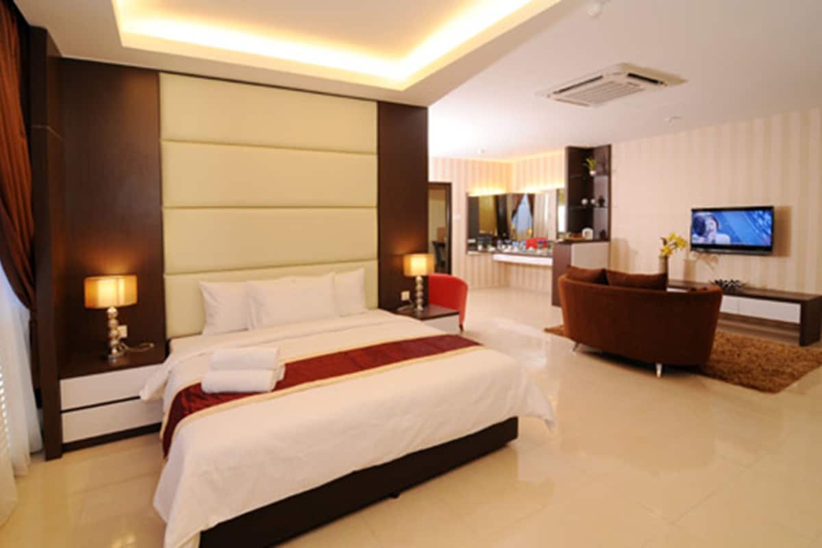 A modern hotel room with a large bed, a TV, a seating area, and a bathroom visible through an open door.