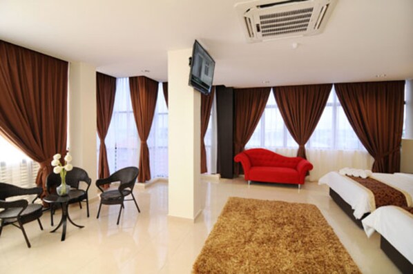 Habitación de hotel con una cama grande, un sofá rojo, un televisor montado en la pared y un amplio ventanal con cortinas.
