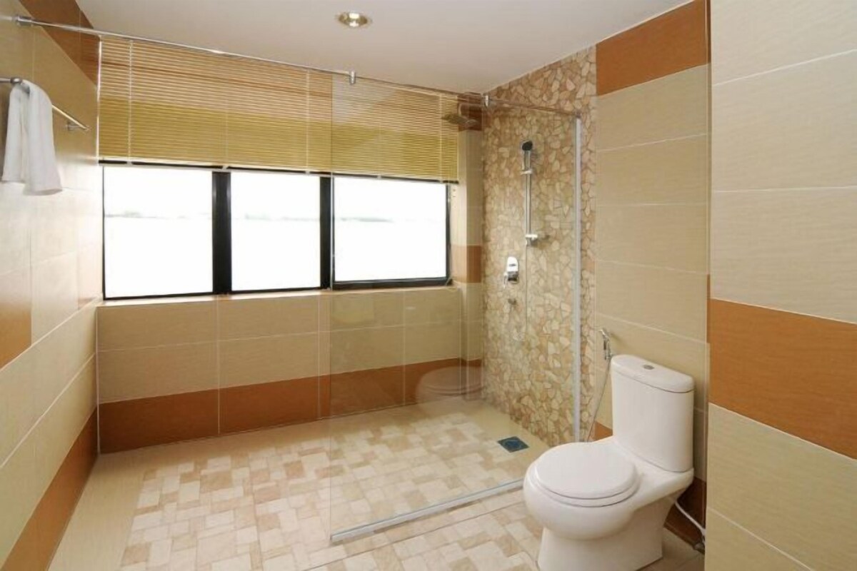 A bathroom with a shower, toilet, and a window with blinds.