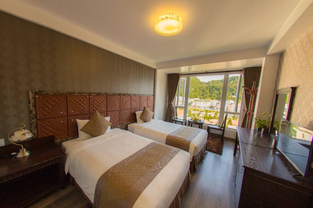 Habitación de hotel con dos camas, un ventanal con vistas, un escritorio y un televisor.