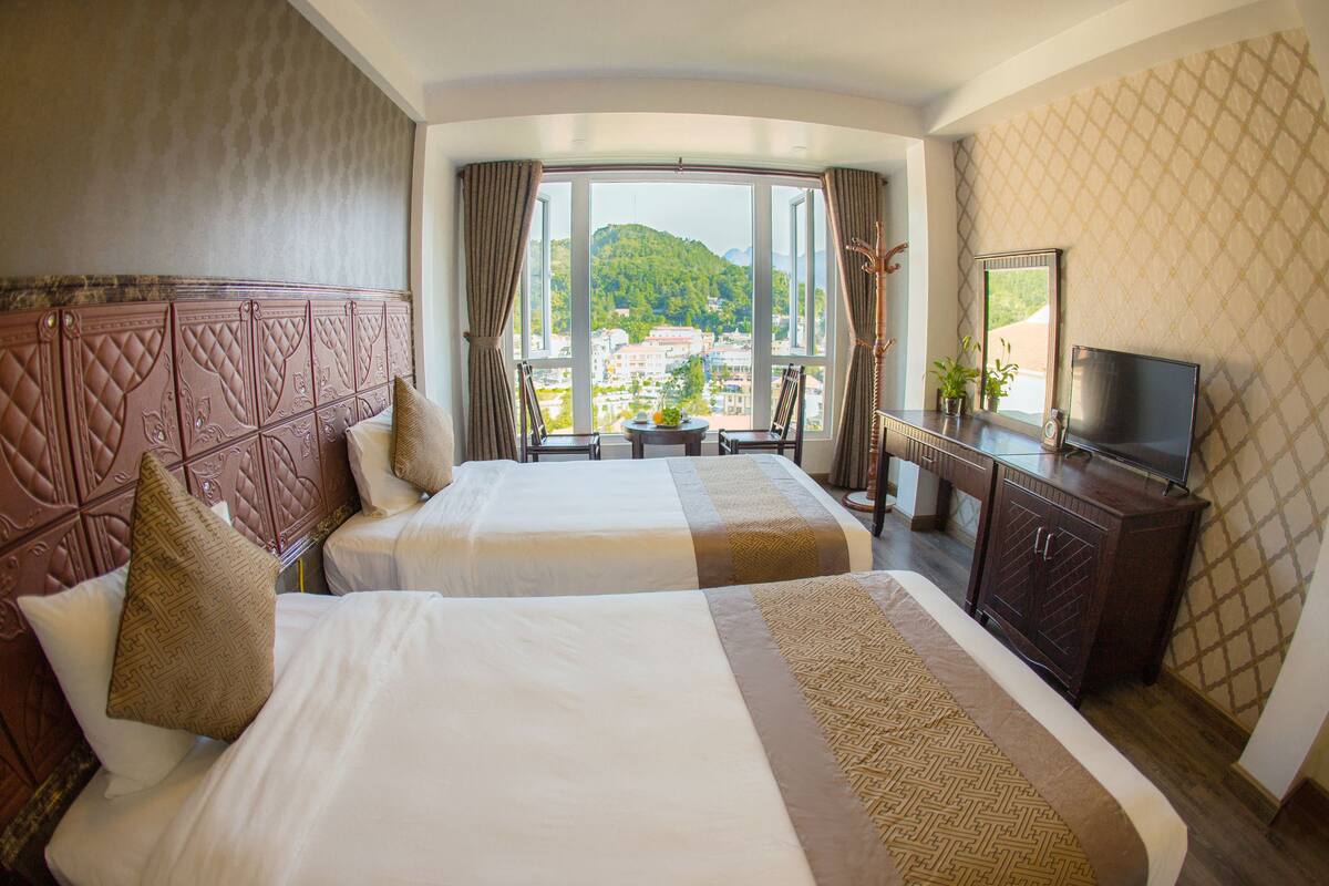 Habitación de hotel con dos camas, televisión y vista a un paisaje urbano.