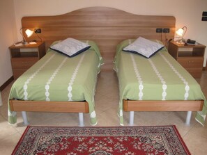 A twin bedroom with two single beds, each with a nightstand, lamp, and a green bedspread. - Locanda Alla Rosa (Lusiana Conco)