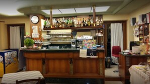 A bar area with a wooden counter, shelves with bottles, a clock, and a red chair. - Locanda Alla Rosa (Lusiana Conco)