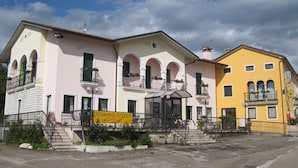 A row of three-story buildings with balconies, a yellow sign indicating a pizzeria, and a clear sky. - Locanda Alla Rosa (Lusiana Conco)