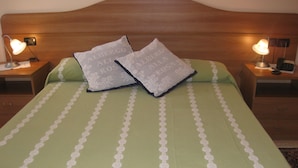 A neatly made bed with green bedding and white floral patterns, two pillows, and two bedside lamps on wooden nightstands. - Locanda Alla Rosa (Lusiana Conco)