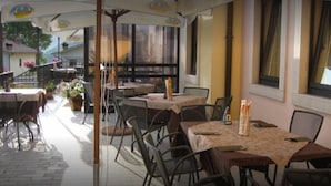 An outdoor cafe with tables and chairs, covered by umbrellas, and a view of the surrounding buildings. - Locanda Alla Rosa (Lusiana Conco)