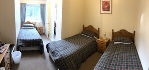 A bedroom with three single beds, a wooden dresser, a bedside table with a lamp, and a window with curtains. - The New Inn Guest House (Bridgend)