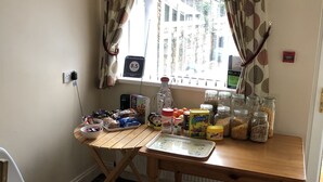 A kitchen area with a table, a chair, and various kitchen items. - The New Inn Guest House (Bridgend)
