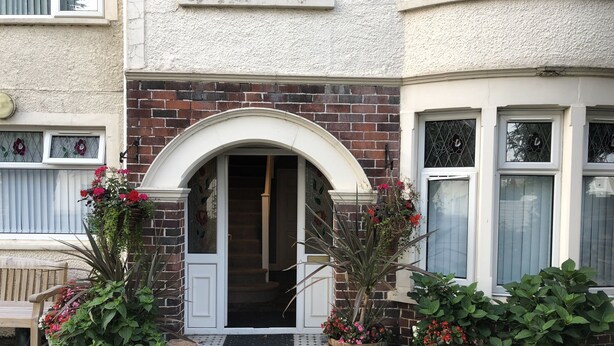 A residential building with a brick facade, a white arched entrance, and potted plants with flowers. - The New Inn Guest House (Bridgend)