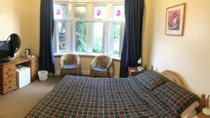 A bedroom with a bed, a wardrobe, a television, a chair, and a window with curtains. - The New Inn Guest House (Bridgend)
