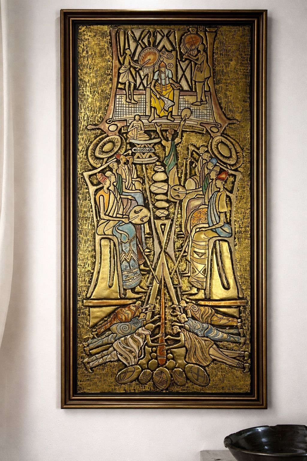 A framed artwork with a central figure and symmetrical design, mounted on a wall.