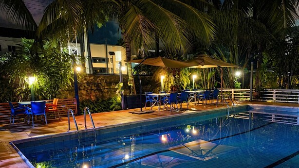 Una piscina con borde de baldosas, rodeada de palmeras y mobiliario exterior.