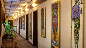 Un pasillo con obras de arte enmarcadas en las paredes, un área de comedor con sillas de mimbre y una alfombra estampada.