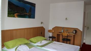 A hotel room with a bed, two chairs, a desk, and a painting of a coastal landscape.