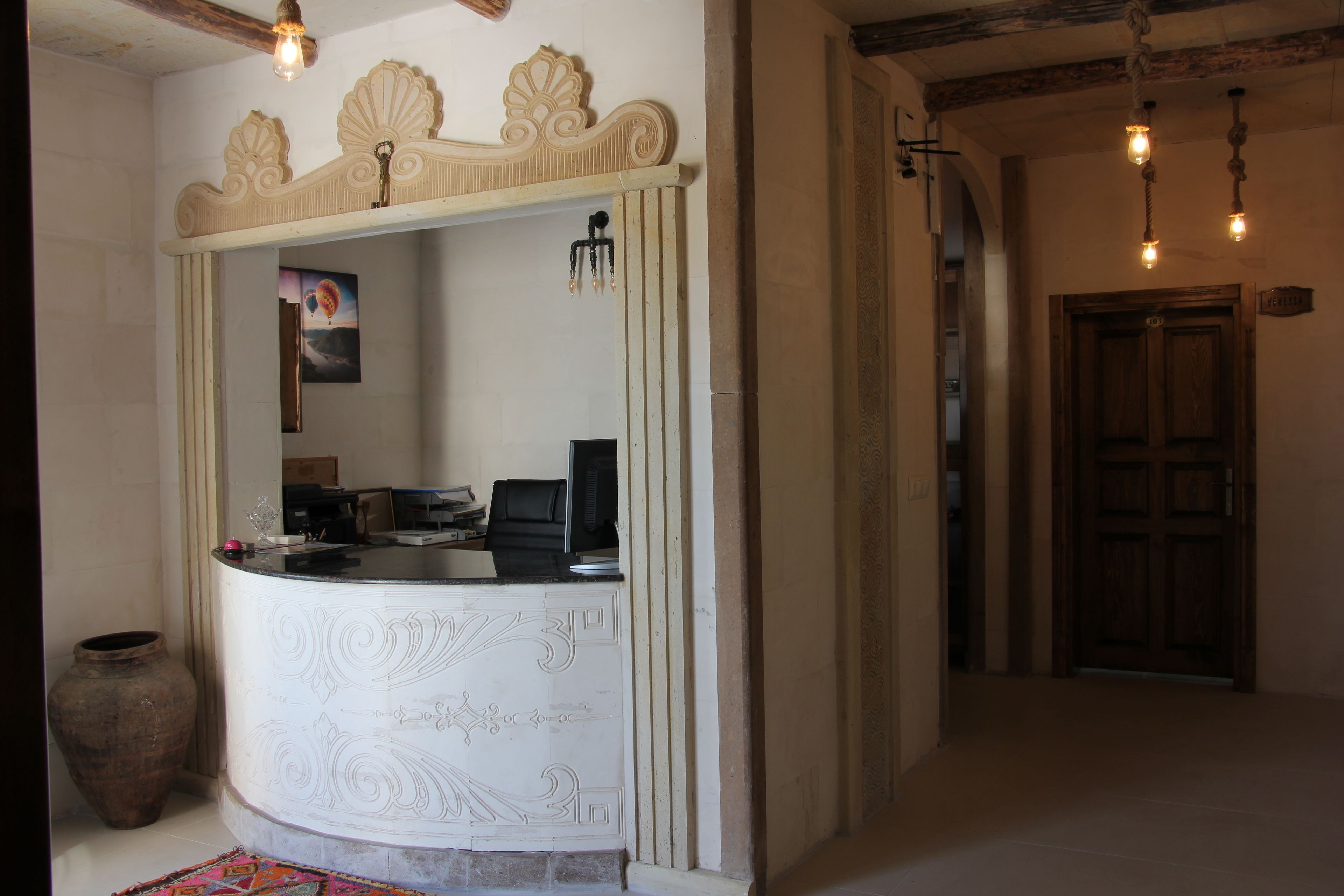 A reception desk with a decorative white panel, a large vase, and a framed picture on the wall.