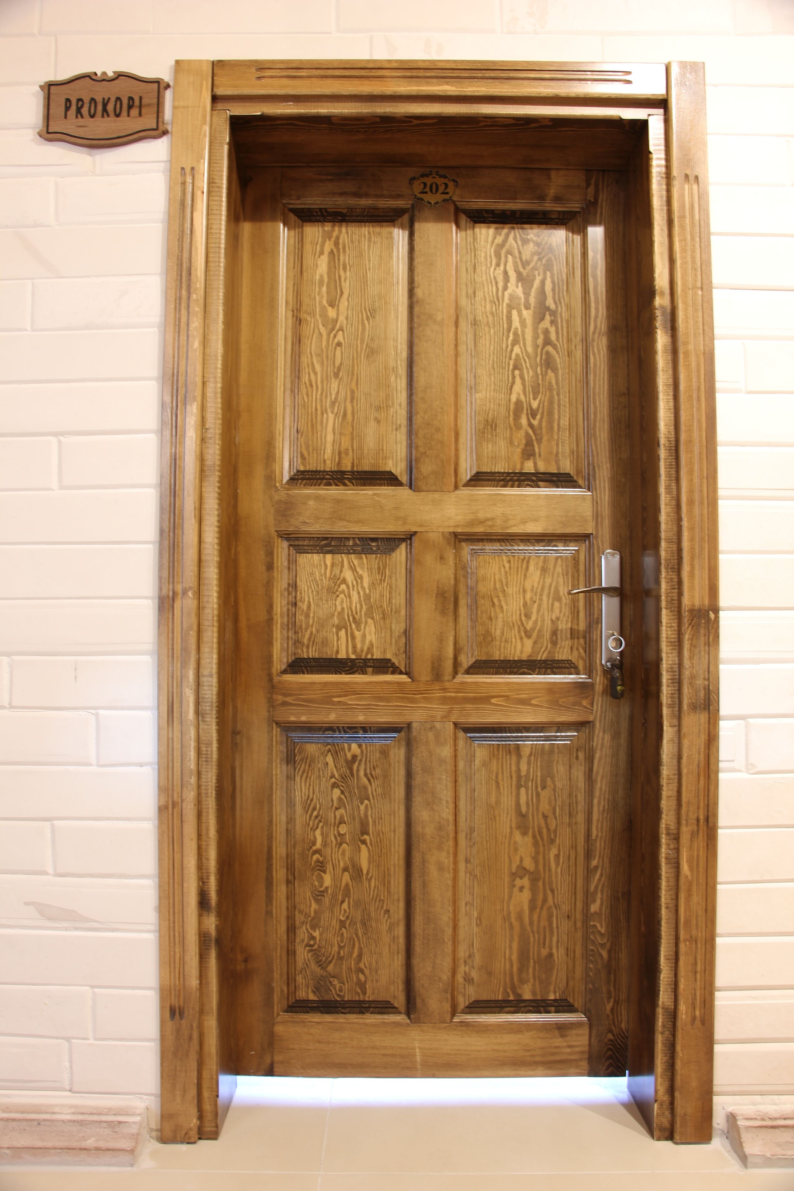 A wooden door with a number plate, a metal handle, and a sign above it.