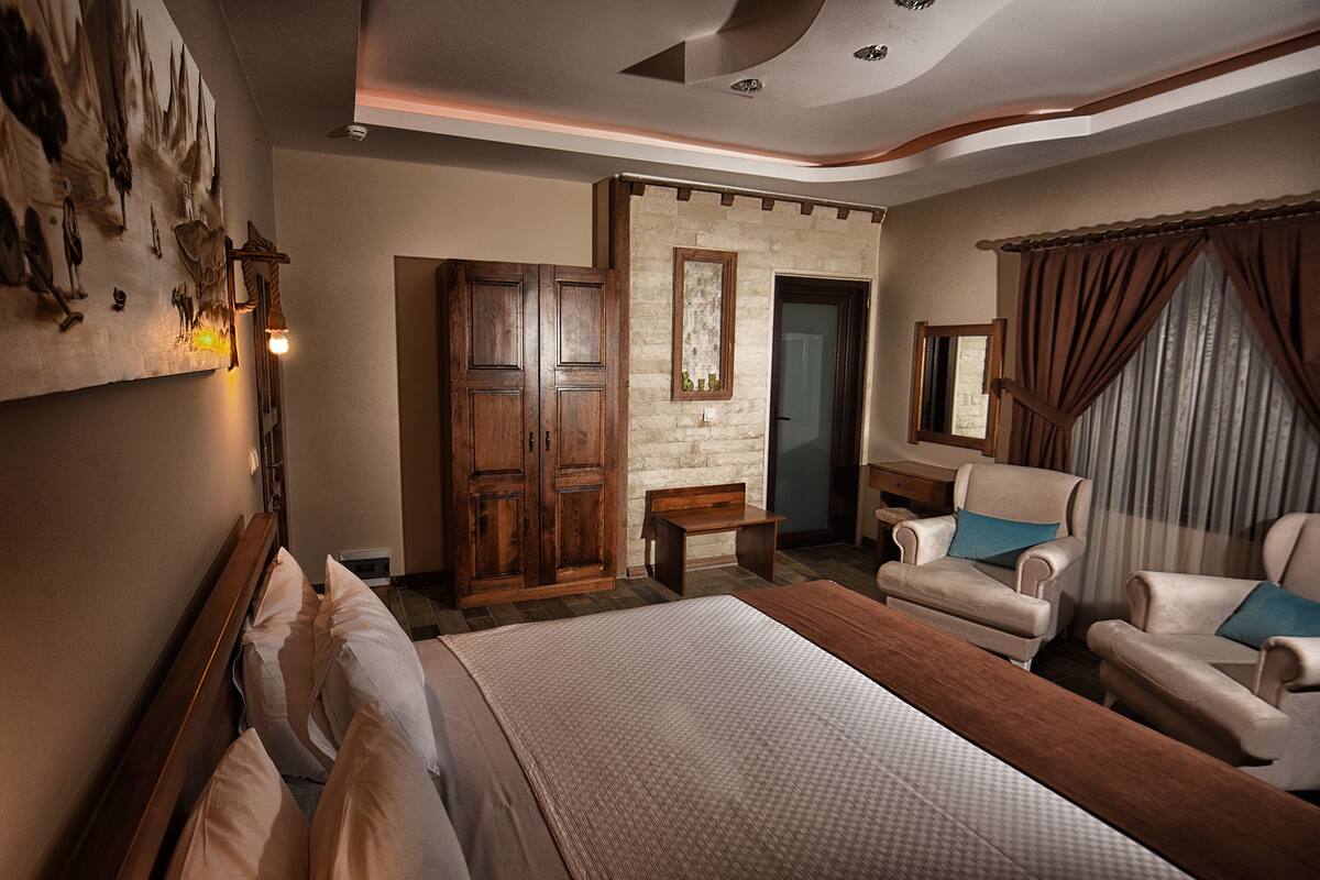 A spacious bedroom with a large bed, a wooden wardrobe, a desk, and two armchairs.