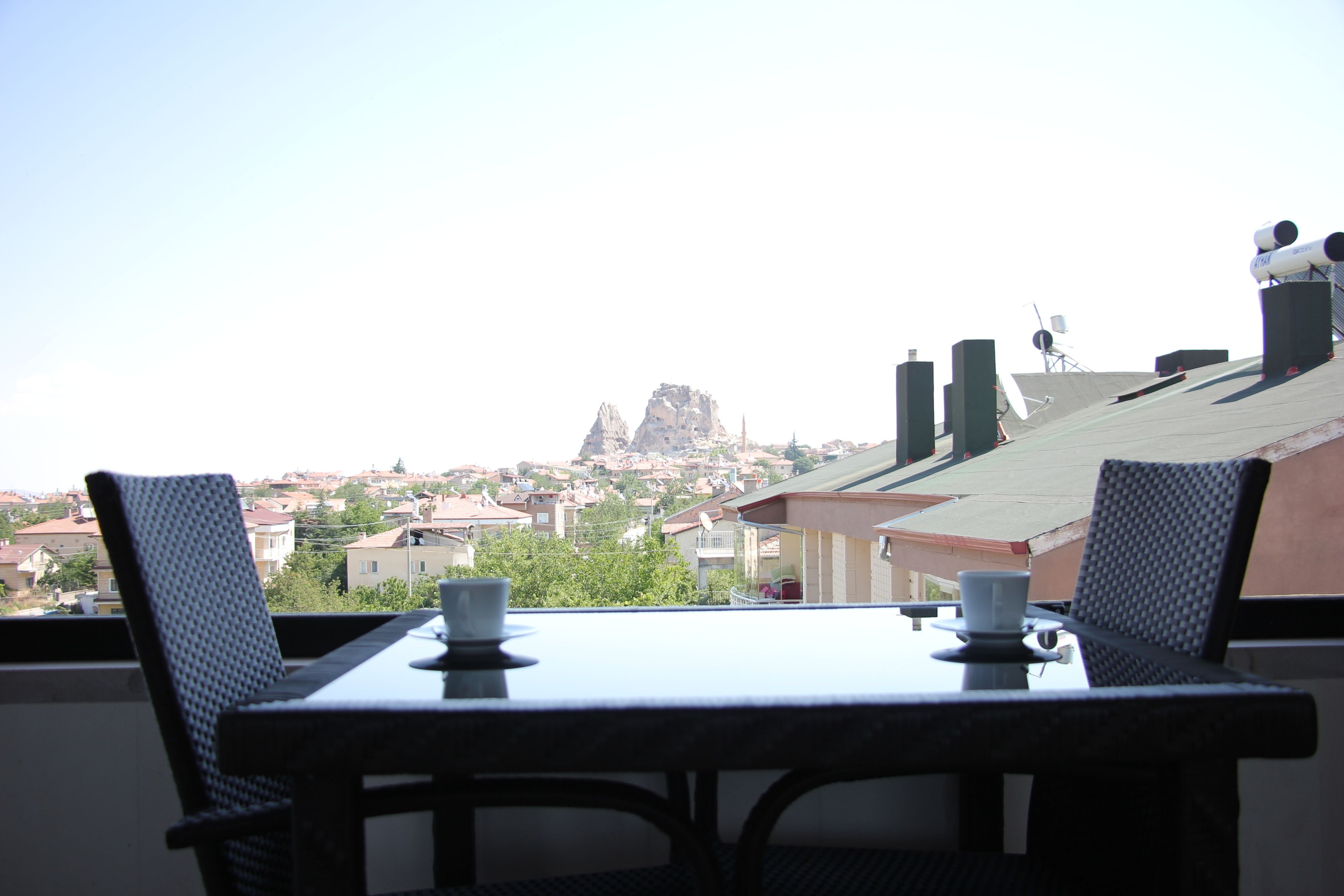 A balcony with a table and chairs, overlooking a residential area with houses and a prominent rock formation.
