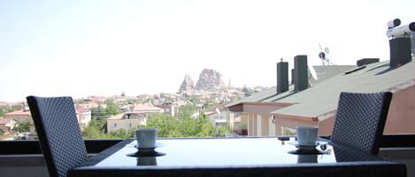 A balcony with a table and chairs, overlooking a residential area with houses and a prominent rock formation.