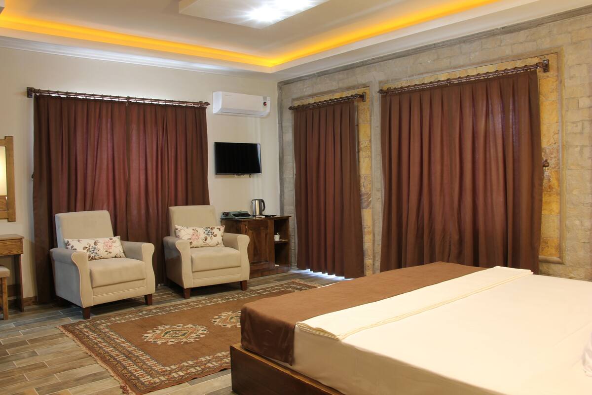 A hotel room with a bed, two armchairs, a television, and a coffee maker.