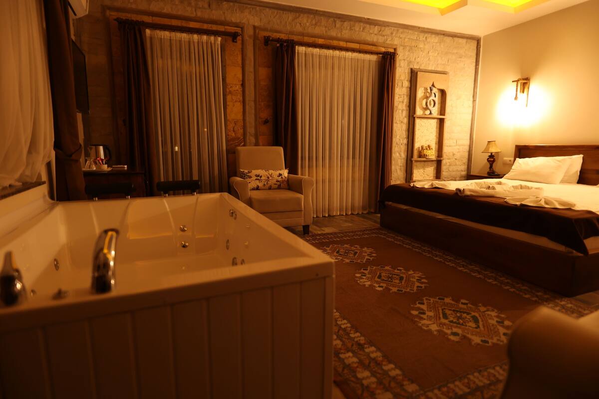 A hotel room with a large bathtub, a bed, a chair, and a nightstand with a lamp.