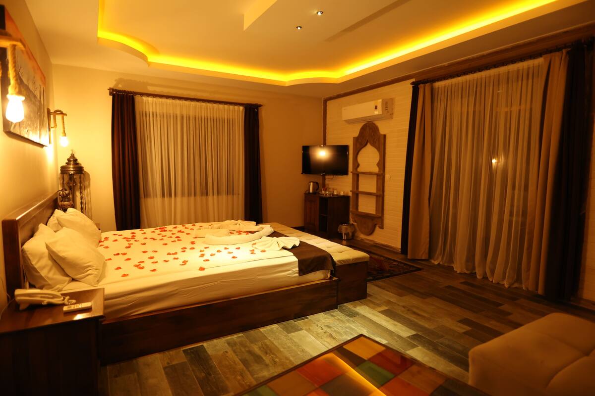 A hotel room with a large bed, a bedside table with a lamp, a TV, and curtains.