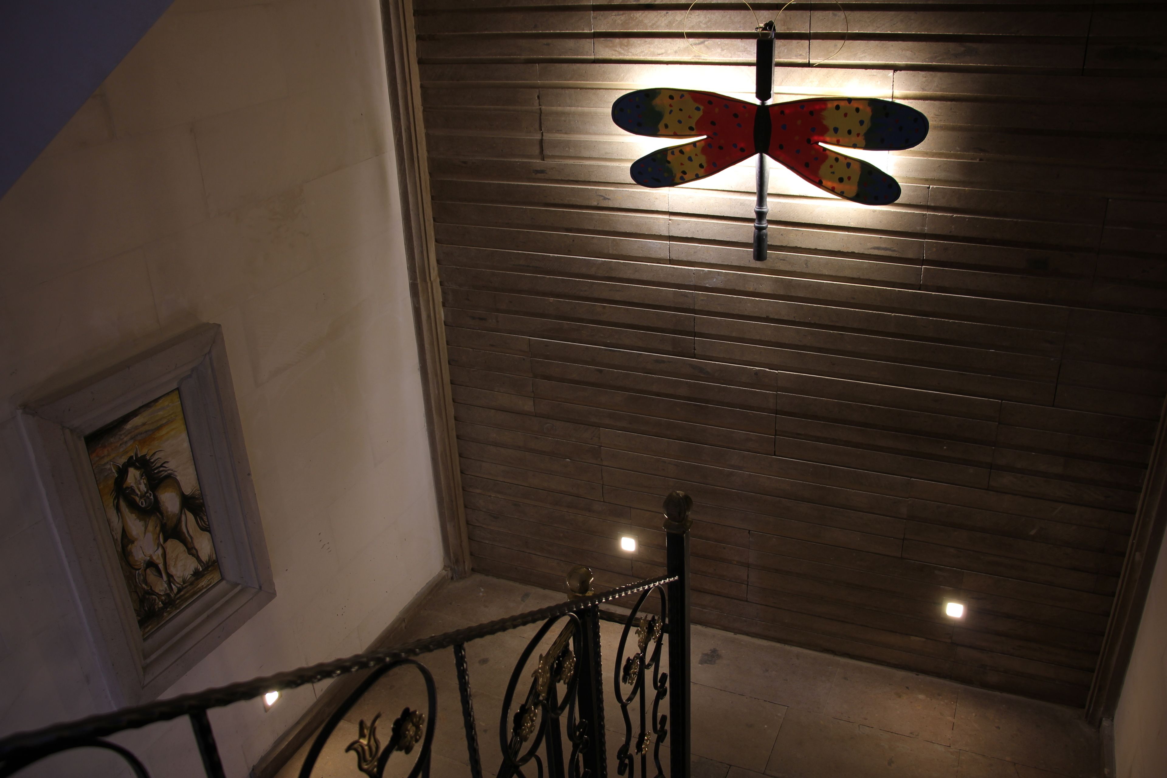 Una escalera con barandilla metálica, techo de madera y un aplique en la pared.