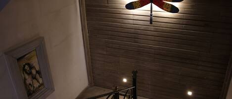 A staircase with a metal railing, a wooden ceiling, and a wall-mounted light fixture.