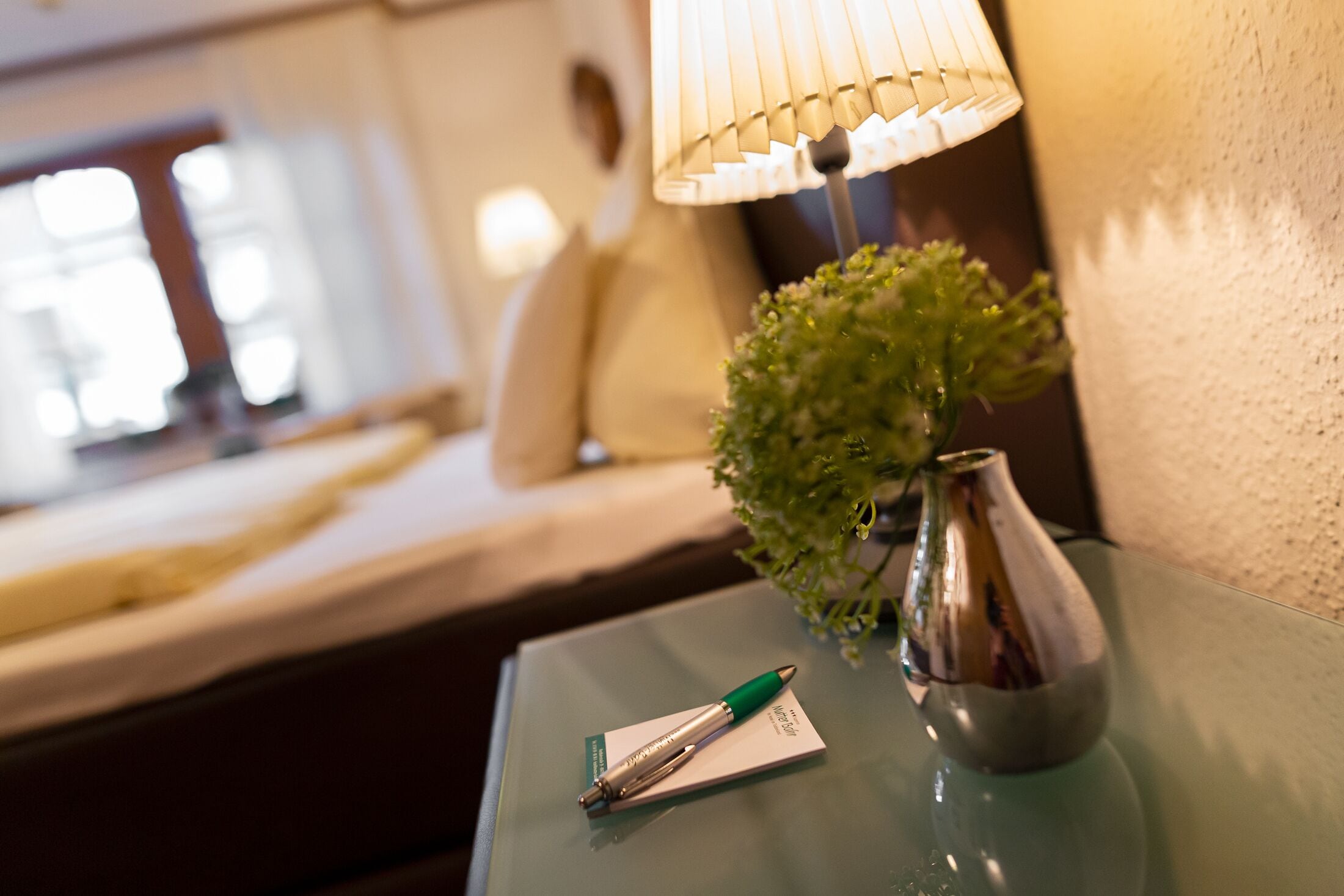 A glass table with a pen, a small plant, and a lamp.