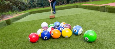 Un jeu de plein air qui se joue sur une pelouse, avec des boules numérotées et un joueur qui utilise un maillet.
