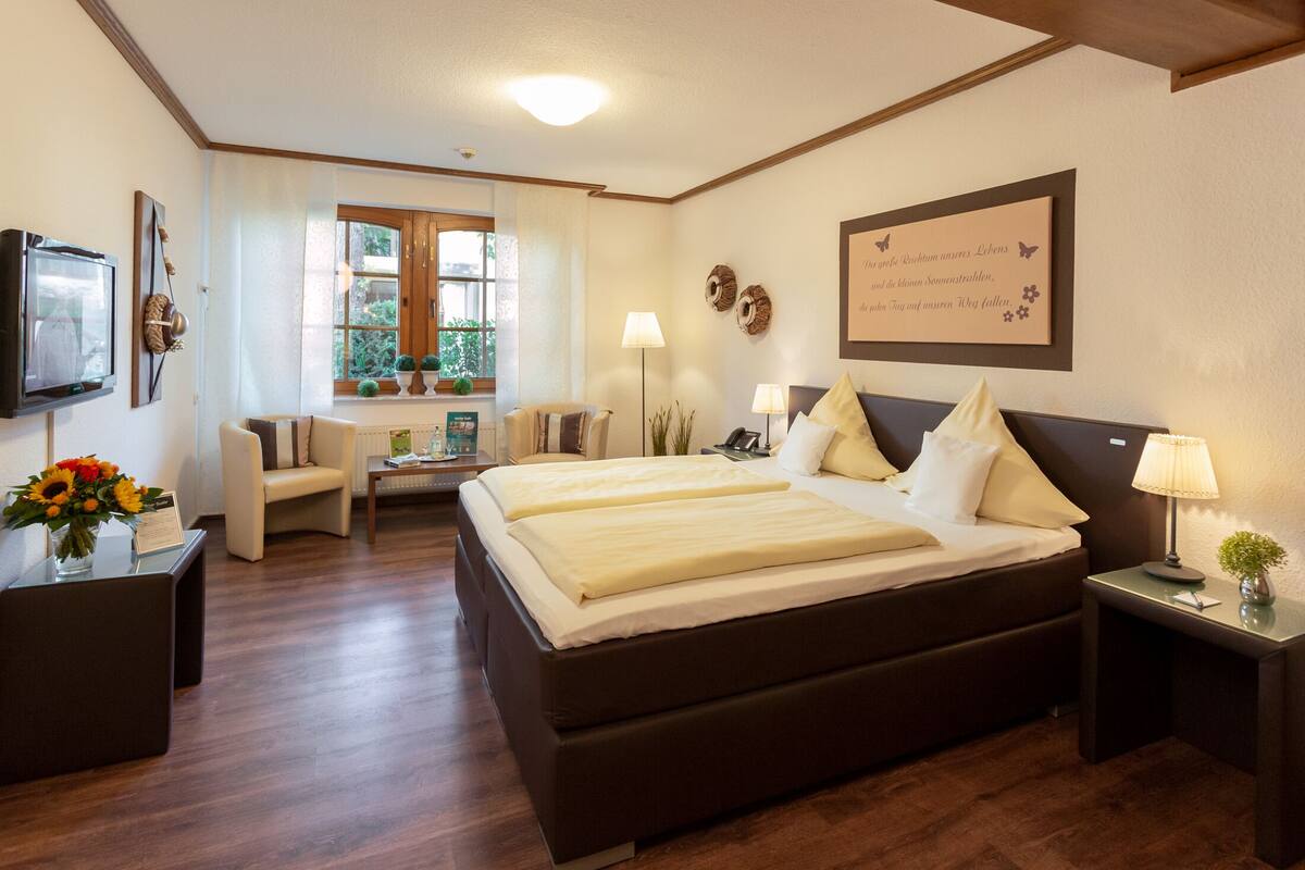 A hotel room with a large bed, a desk with a computer, a chair, and a window with curtains.