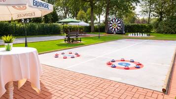 A dartboard, a table with a green umbrella, and a bench in a park setting.