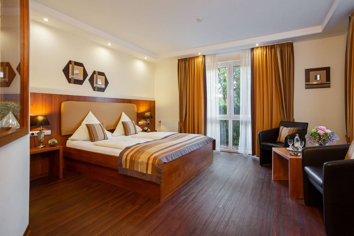 A hotel room with a large bed, a sofa, a small table, and a window with curtains.