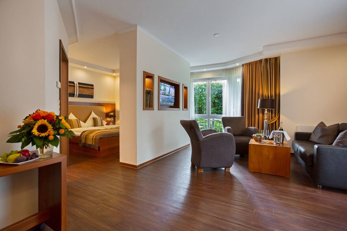 A modern hotel room with a bed, a sofa, a coffee table, and a TV.