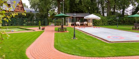 A courtyard with a curling rink, green lawns, and a pavilion with tables and umbrellas.