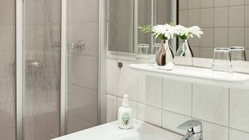 Une salle de bain moderne avec une douche à parois de verre, un grand miroir et un lavabo blanc doté d’un robinet chromé.