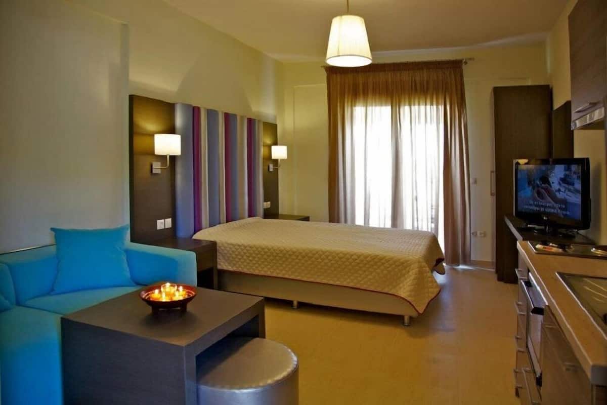 A hotel room with a bed, a sofa, a TV, and a desk with a lamp.